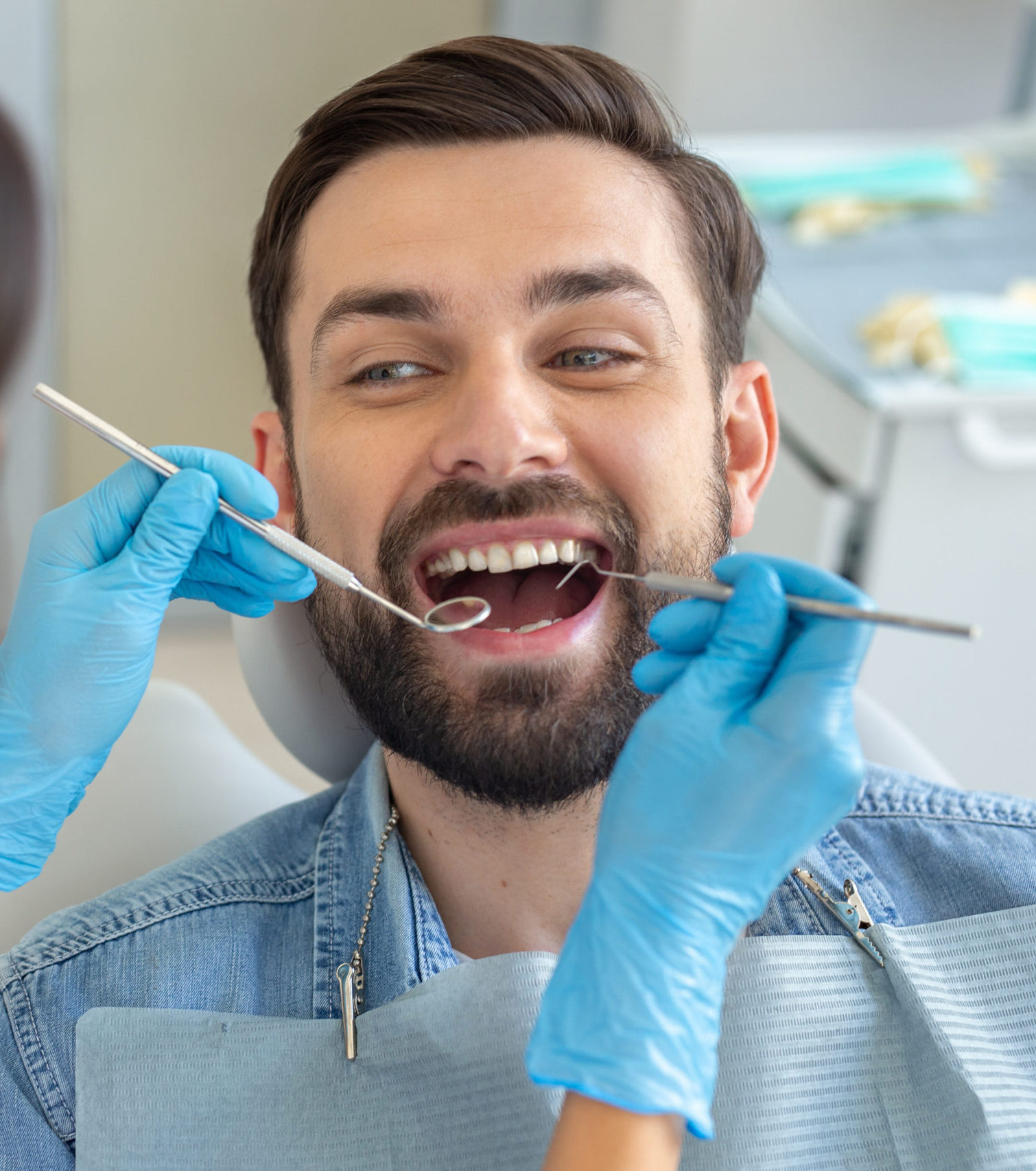 dentist examining teeth of handsome smiling client in dental chair