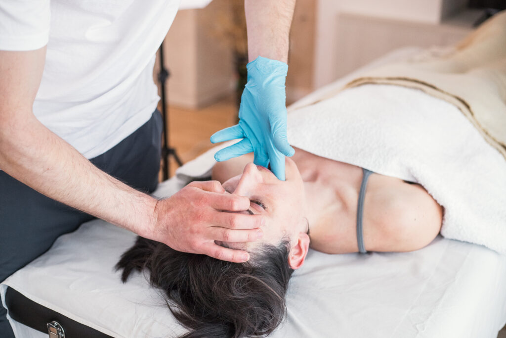 Osteopathic therapist doing treatment to Caucasian woman with jaw problem, mandibular alignment. Treatment to relieve pain and improve the patient's health conditions.