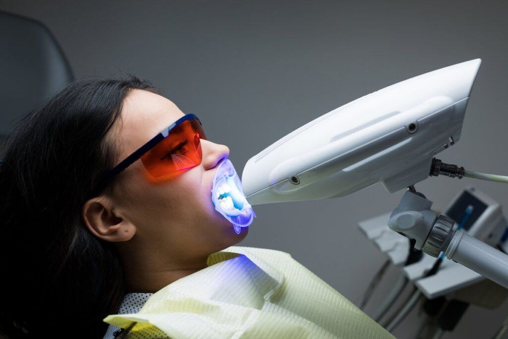 Close-up portrait of female patient at dentist in the clinic. Teeth whitening procedure with ultraviolet light UV lamp.